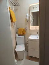 Bathroom through the doorway with toilet, yellow towels, wall hairdryer and drawer vanity basin